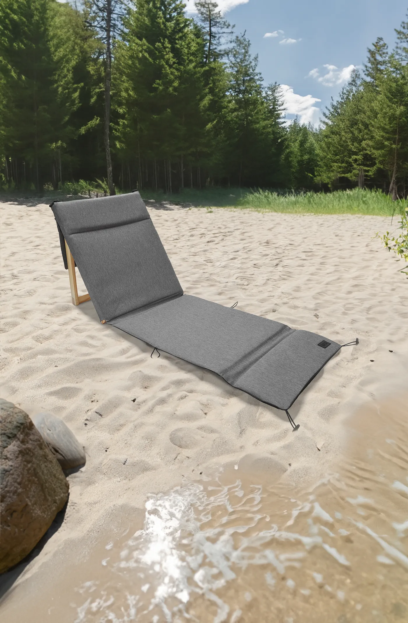 Silla de playa plegable gris con respaldo de madera, sobre la arena junto al agua